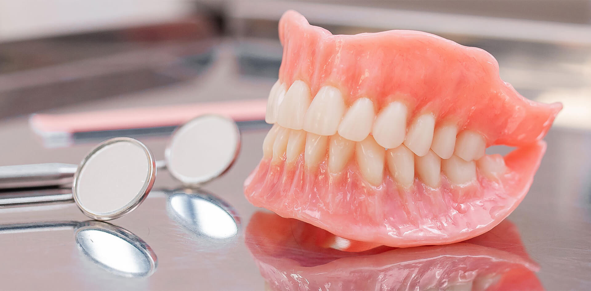 Dentures displayed on a dental tray alongside dental mirrors, representing restorative dentistry services offered by PGA Dentistry in Palm Beach Gardens.