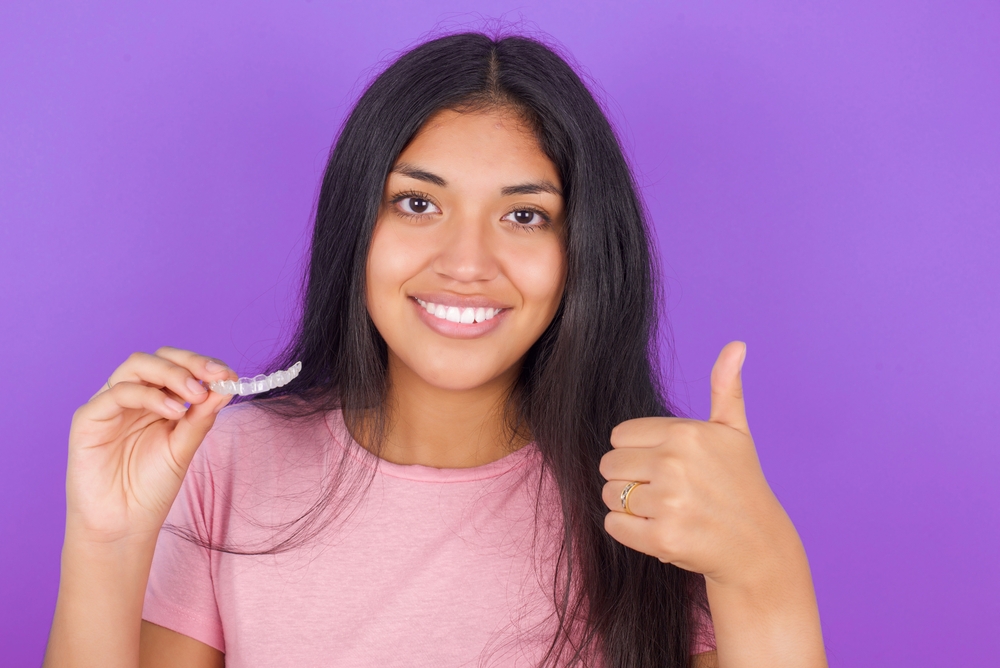 young girl holding Invisalign clear aligners while giving a thumbs up