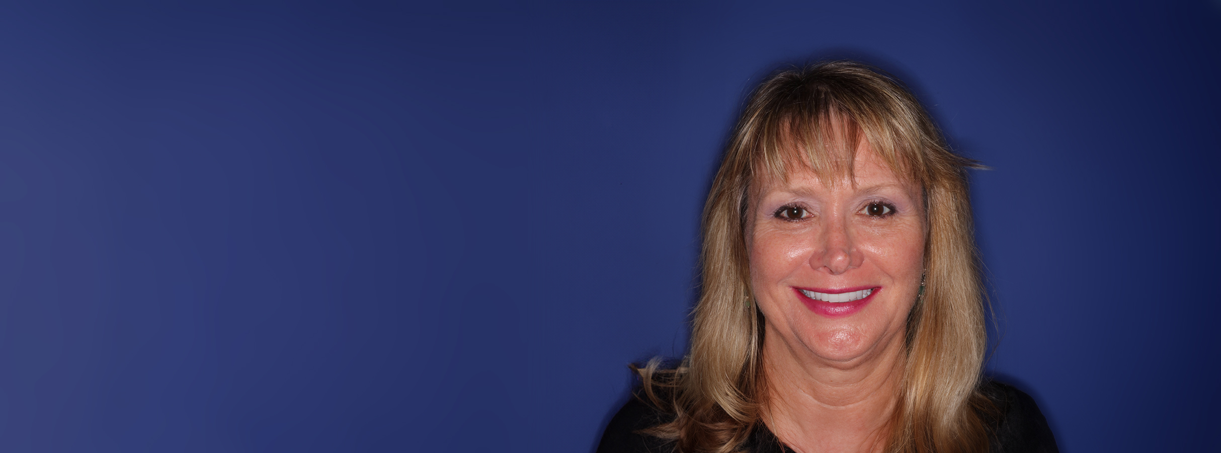 Janice smiling after full mouth reconstruction with crowns, showcasing restored dental health and confidence against a dark blue background.